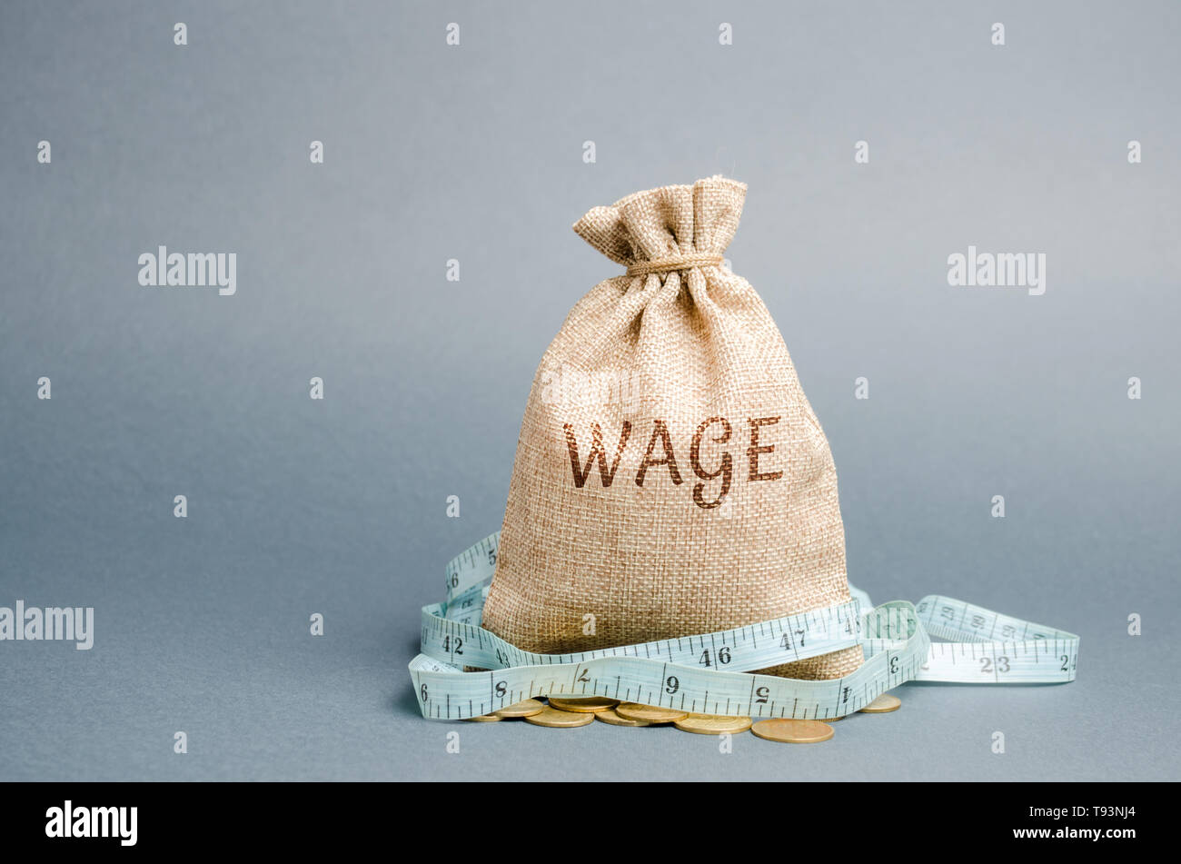 Money bag with the word Wage and tape measure. Wage cuts. The concept of limited profit. Lack of money and poverty. Small income. Salary reduction. Un Stock Photo