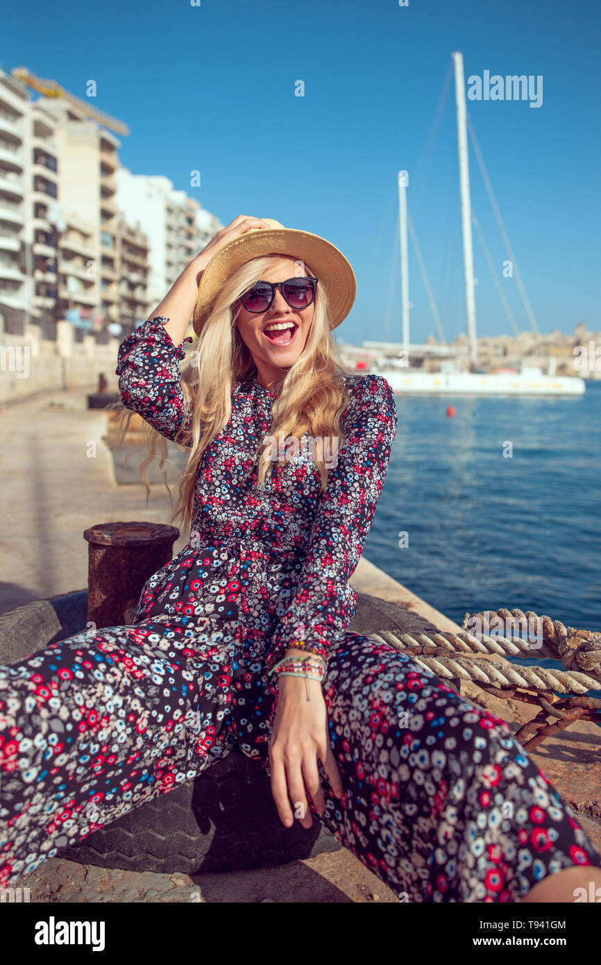 Happy fashionable mediterranean woman in hat laughing at harbour dock Stock Photo