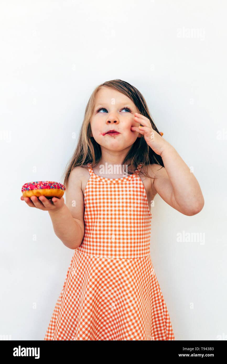 portrait of a little girl in love with her doughnut. She is holding a doughnut on her hand and looking to the sky with a satisfied expression Stock Photo