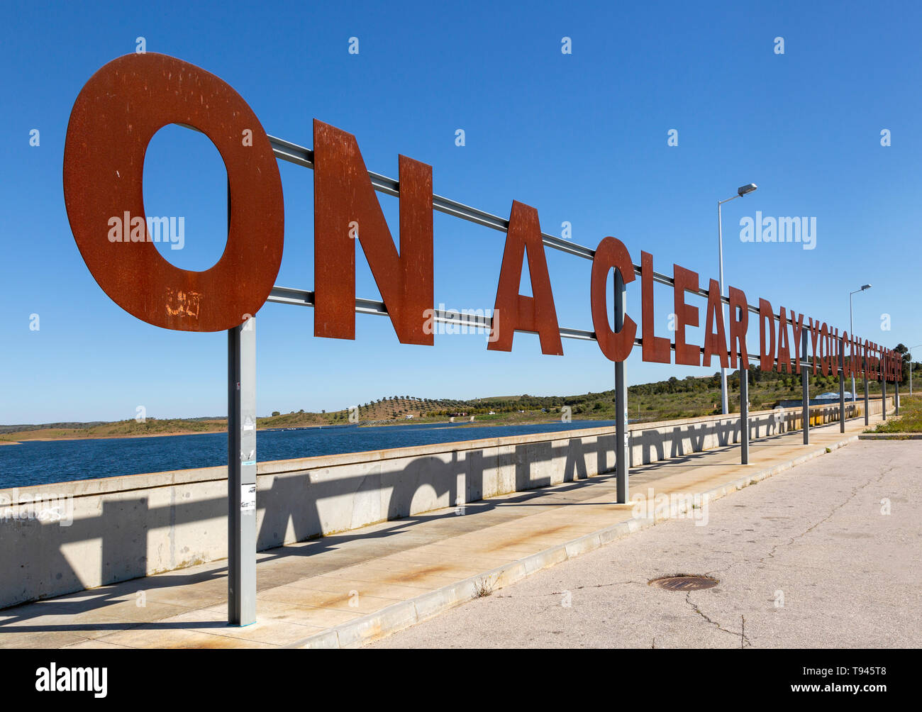 Large red rusty capital letters ON A CLEAR DAY  YOU CAN SEE FOREVER blue sky background, Alqueva dam, Moura, Portugal Stock Photo