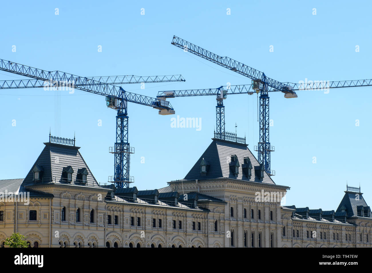 Several working tower cranes over the roof of a Gothic building against a blue sky Stock Photo