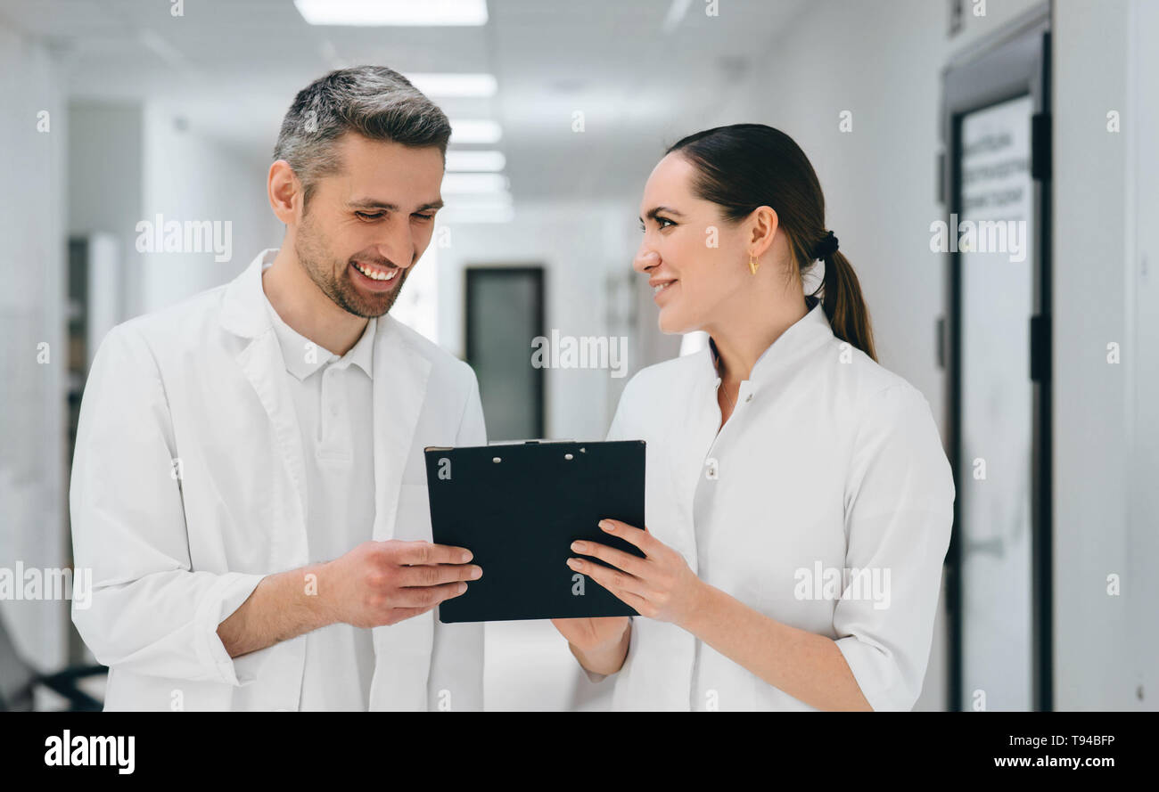 Two doctors with clipboard communicate standing at hospital corridor. doctors laughing and having friendly emotions Stock Photo