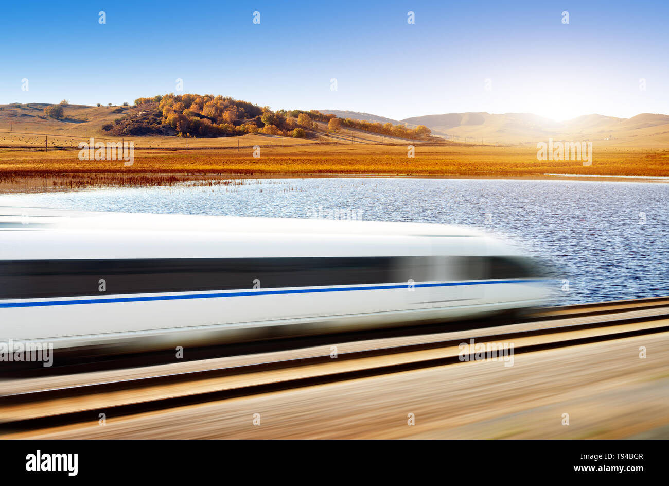 Dynamically blurred high-speed train passing the grassland river Stock Photo