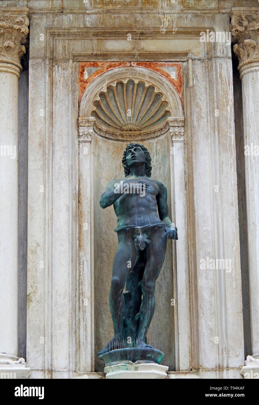 A bronze statue of a naked young man looking heavenward with his right hand on his heart, set in niche painted to give a tromp l’oeil effect Stock Photo
