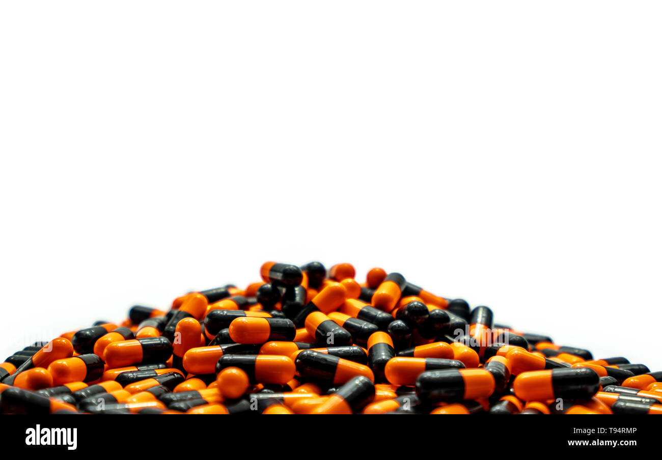 Closeup pile of orange-black capsule pills on white background. Vitamins and supplements. Pharmaceutical industry. Global healthcare concept. Capsule  Stock Photo