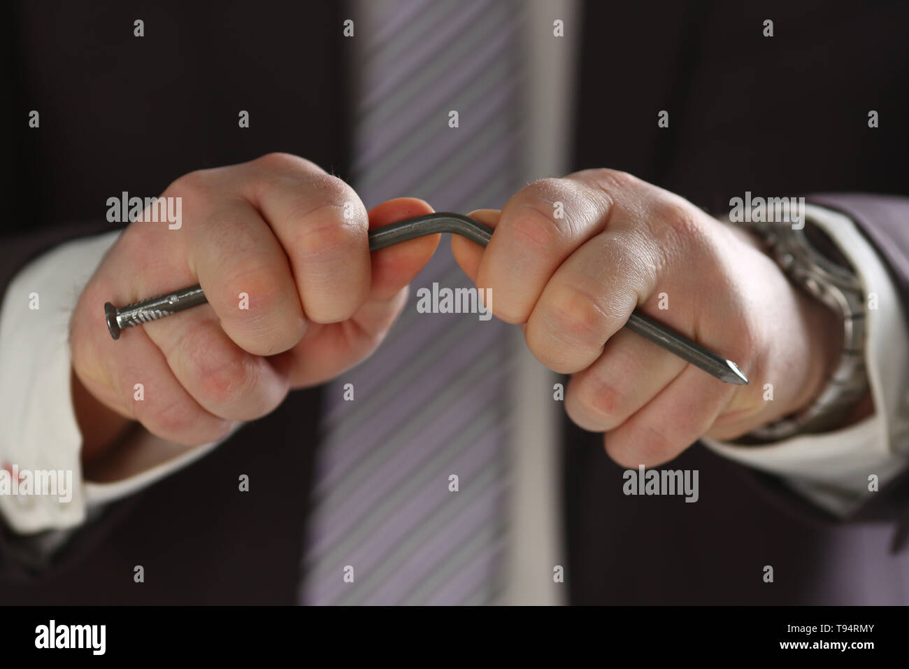 Man in suit and tie bend nail with arms closeup no limit energy easy problem solve issue superman help pressure concept Stock Photo