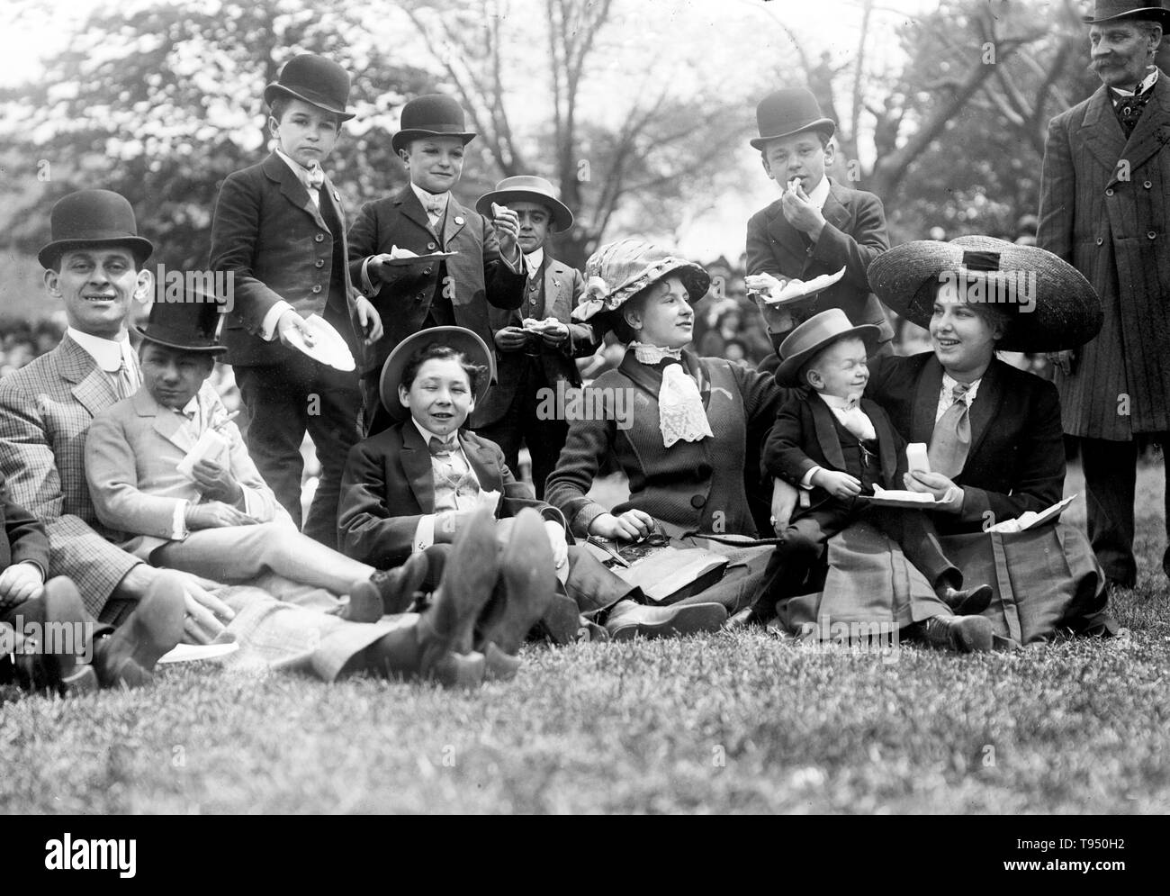 Entitled: 'Midgets May Party - Central Park. Group seated on grass.' Midget is a term for a person of unusually short stature that is considered by some to be pejorative. While not a medical term, it has been applied to persons of unusually short stature, often with the medical condition dwarfism, particularly proportionate dwarfism. Midgets have always been popular entertainers. P. T. Stock Photo