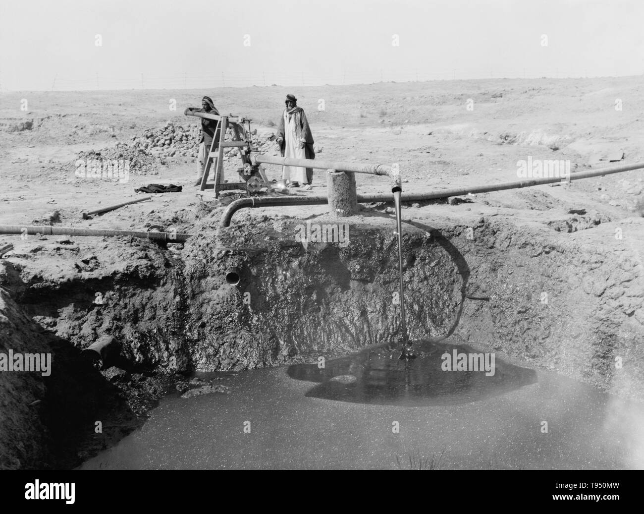 Men pumping bitumen from a well in 1932, in an area of bituminous wells south of Mosul, Iraq. Bitumen is a black viscous mixture of hydrocarbons obtained naturally or as a residue from petroleum distillation. It is used for road surfacing and roofing. Stock Photo