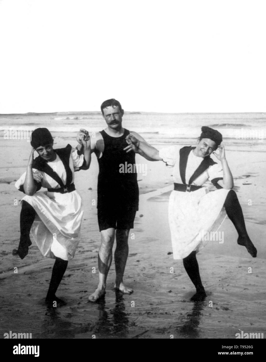 Entitled: 'Bathers' two women and one man wearing bathing suits doing funny pose on beach. Photographed by W.B. Davidson, 1897. Stock Photo