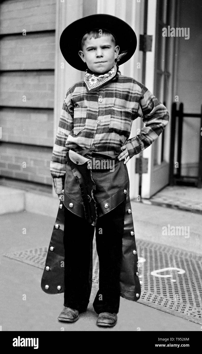 Entitled: 'Boy in cowboy costume'. Many children participate in a form of role-playing known as make believe, wherein they adopt certain roles such as doctor and act out those roles in character. Sometimes make believe adopts an oppositional nature, resulting in games such as cops and robbers. Photographed by Harris & Ewing, 1928. Stock Photo