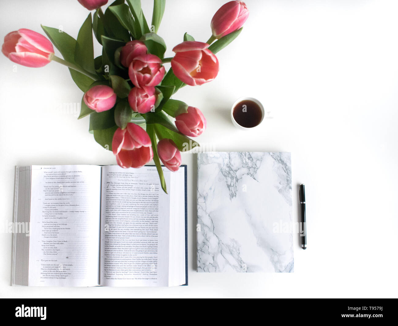 Bible flat lay with red, pink tulip and petals. Open journal, notebook on white background. Additionally: Black tea, black pen, to do list, cross. Stock Photo