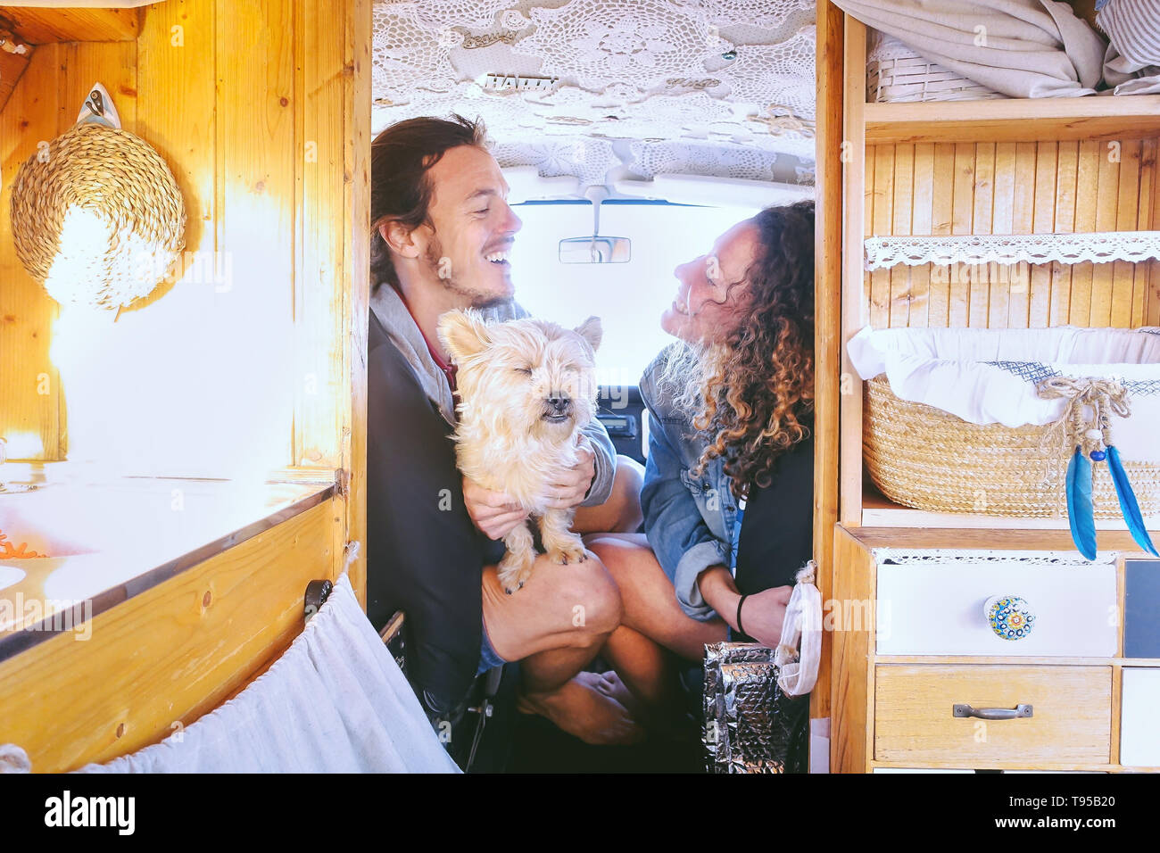 Happy couple having fun in vintage minivan with their dog during a road trip - Young people enjoying time together and laughing in vacation holidays Stock Photo