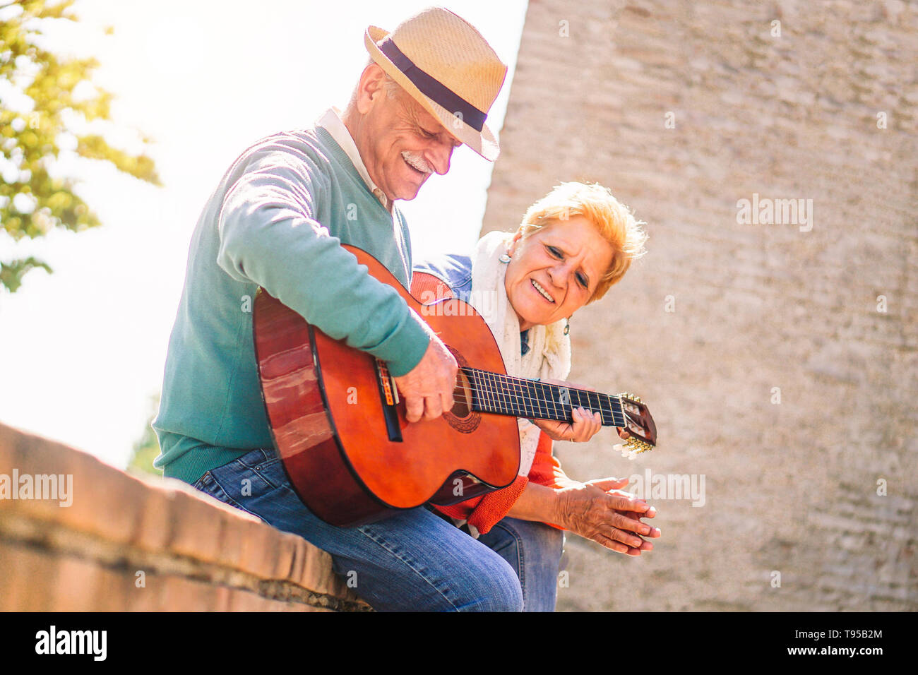 Happy senior couple playing a guitar and having a romantic date outdoor - Mature people having fun enjoying time together in vacation Stock Photo
