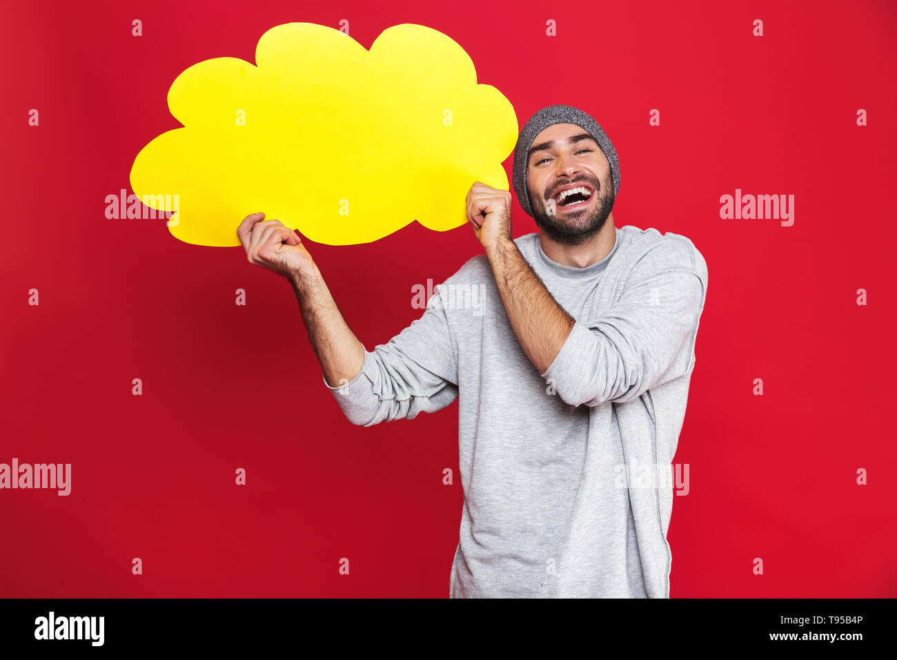 Photo of unshaved man 30s in casual wear smiling and holding blank thought bubble isolated over red background Stock Photo