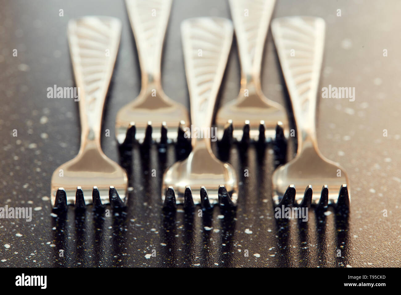 Steel forks on black table. Macro photo for dishware design and kitchen theme. Macro photography of silver forks on table with using focus stacking. Stock Photo