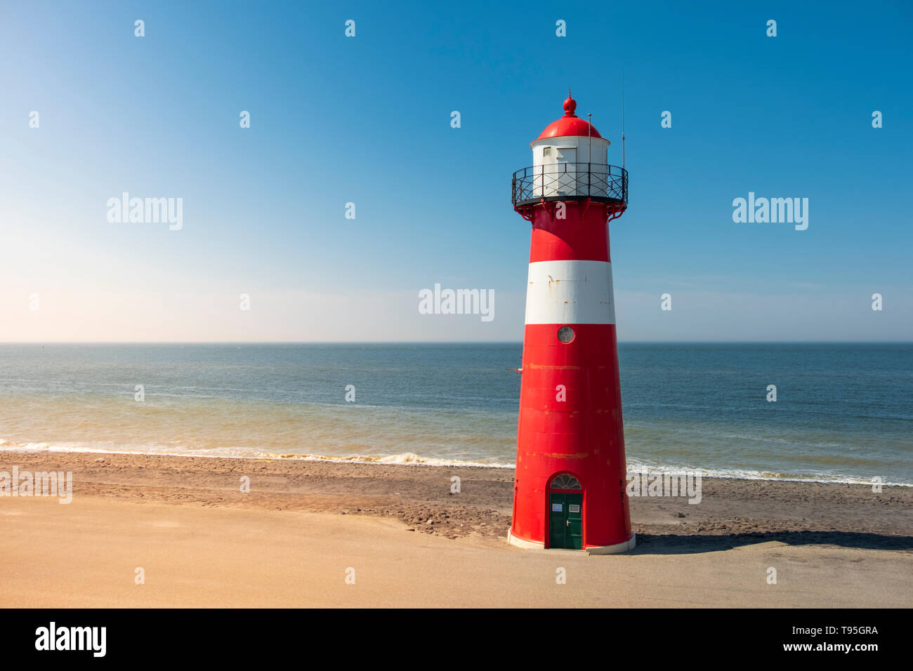 A red and white lighthouse at sea under a clear blue sky near Westkapelle in Zeeland, The Netherlands. Stock Photo