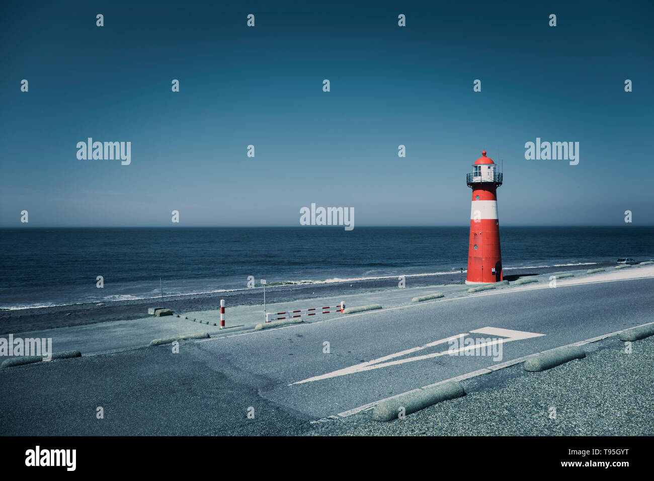 A red and white lighthouse at sea under a clear blue sky near Westkapelle in Zeeland, The Netherlands. Stock Photo