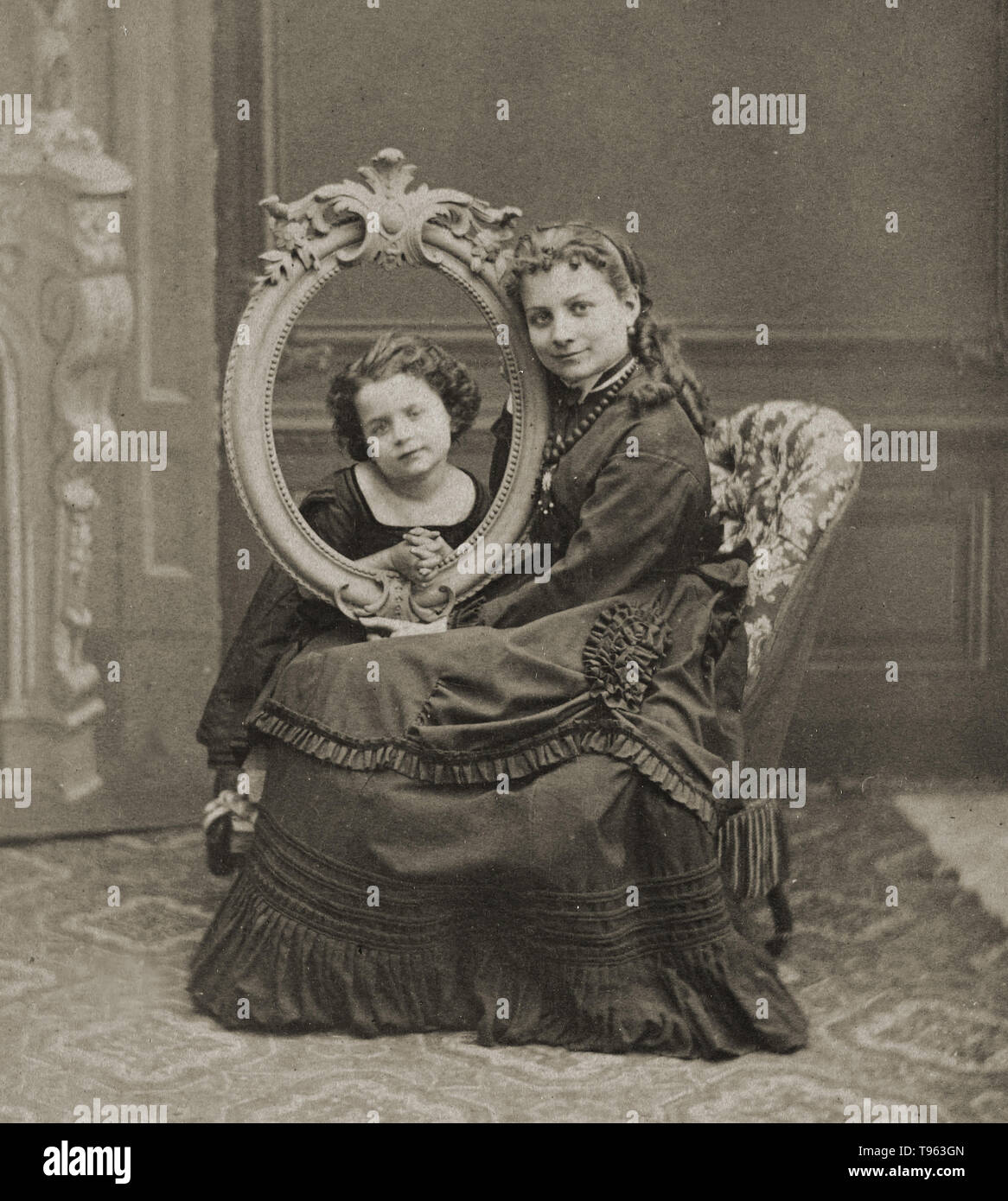 Young woman posing with child, c. 1870. The child's head is being viewed through an empty picture frame. Apart from demonstrating a mother's loving focus on her child, the prop draws attention to the historical shift in portraiture from the medium of painting to photography. E. Thiebault, French. Albumen silver print. Stock Photo