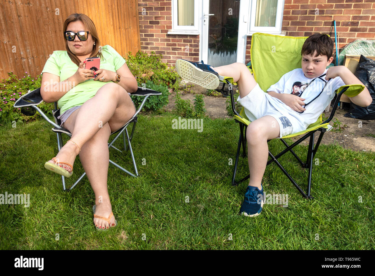Portrait of a mother and son sat in a folding chair, relaxing in the garden. Stock Photo
