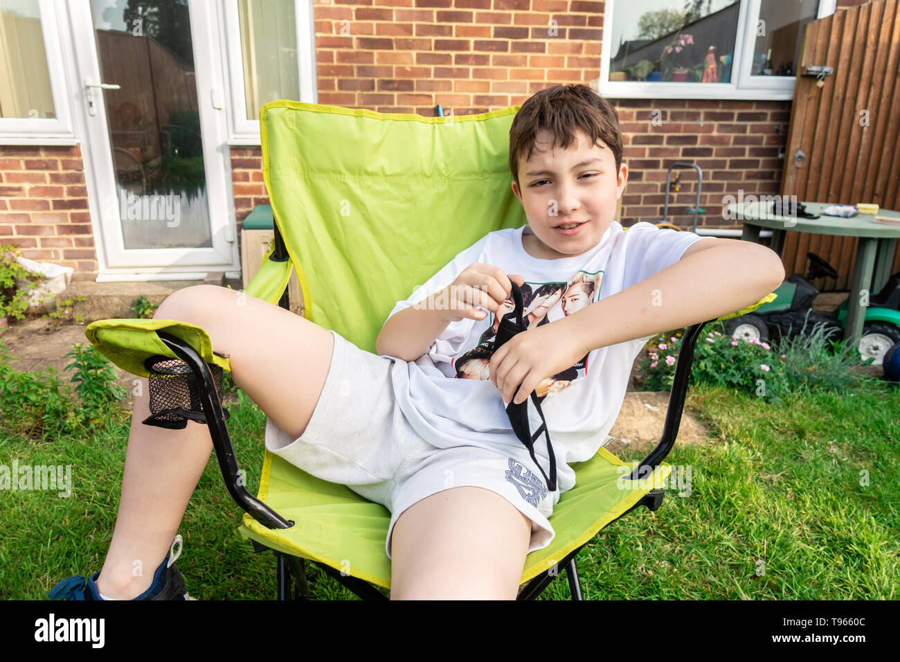 Portrait of a boy sat in a folding chair, relaxing in the garden. Stock Photo