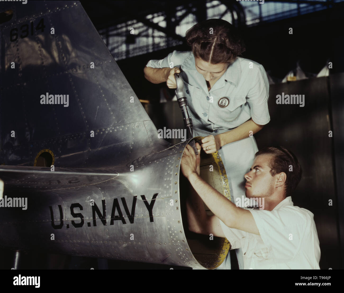 Mrs. Virginia Davis, a riveter in the assembly and repair department of the Naval air base, supervises Charles Potter, a NYA trainee from Michigan, Corpus Christi, Texas. After eight weeks of training he will go into civil service. Should he be inducted or enlist in the armed service, he will be valuable to mechanized units of the Army or Navy. Stock Photo