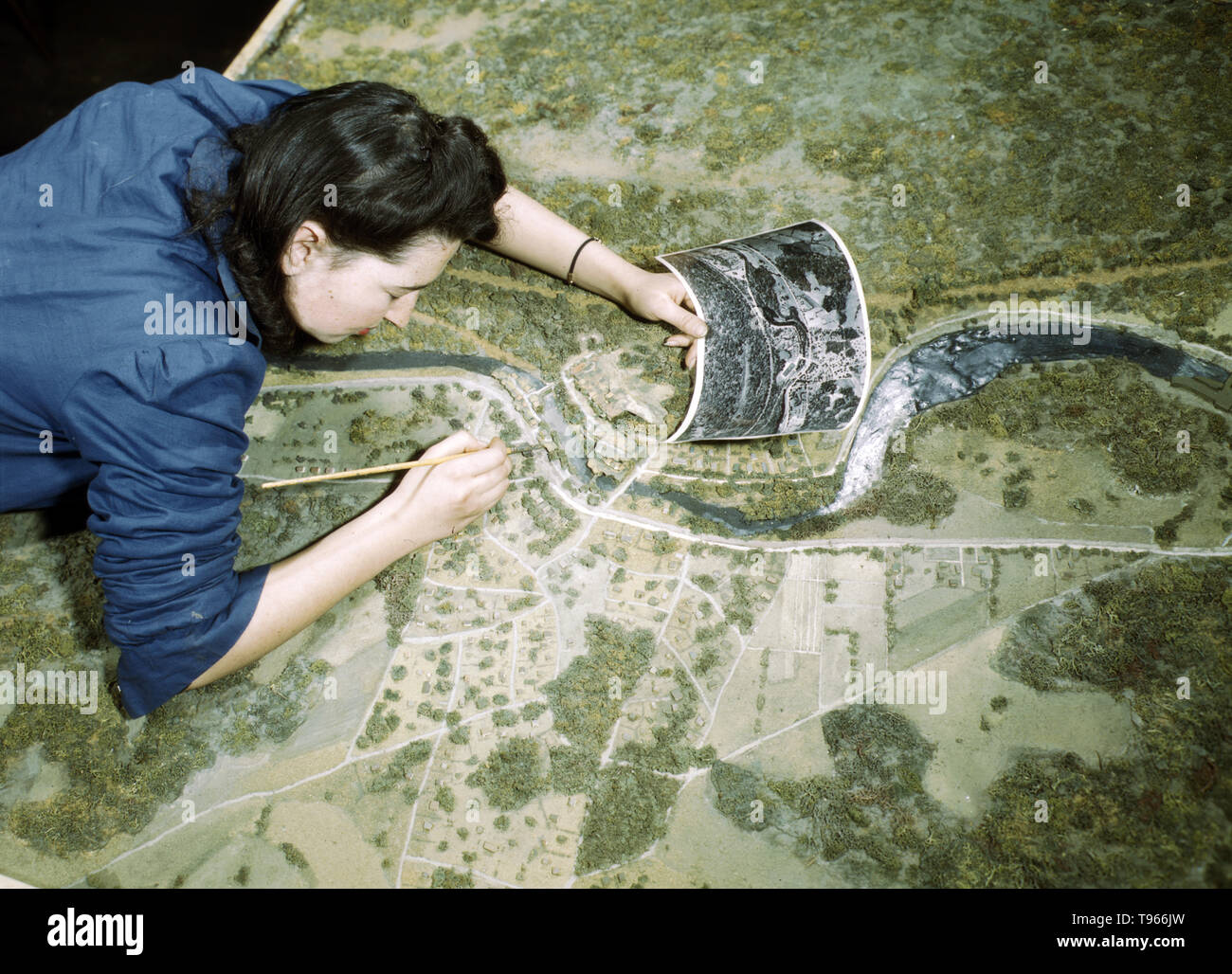 Camouflage class at New York University, where men and women are preparing for jobs in the Army or in industry, New York, N.Y. This model has been camouflaged and photographed. The girl is correcting oversights detected in the camouflaging of a model defense plant  Photographed by Marjory Collins, 1943. Stock Photo