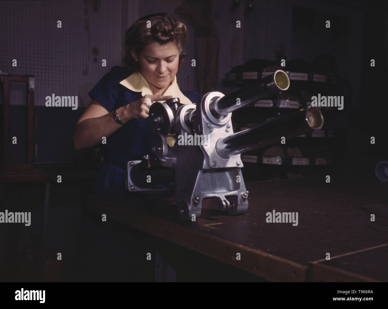 A young woman employee of North American Aviation, Incorporated, working over the landing gear mechanism of a P-51 fighter plane, Inglewood, California. The mechanism resembles a small cannon. Although the image of 'Rosie the Riveter' reflected the industrial work of welders and riveters, the majority of working women filled non-factory positions in every sector of the economy. What unified the experiences of these women was that they proved to themselves, and the country, that they could do a man's job and could do it well. Photographed by Alfred T. Palmer, 1942. Stock Photo