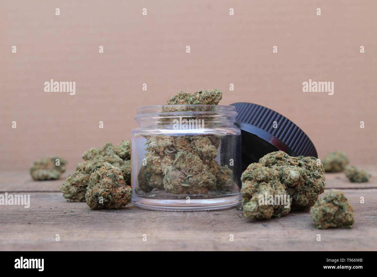 Open Glass Jar of Marijuana Sitting on Table Surrounded by Cannabis Buds Stock Photo