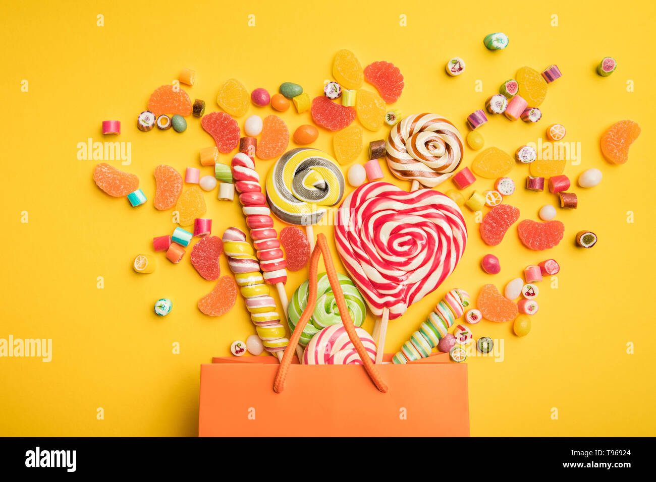 top view of tasty multicolored candies scattered from paper bag on bright yellow background Stock Photo
