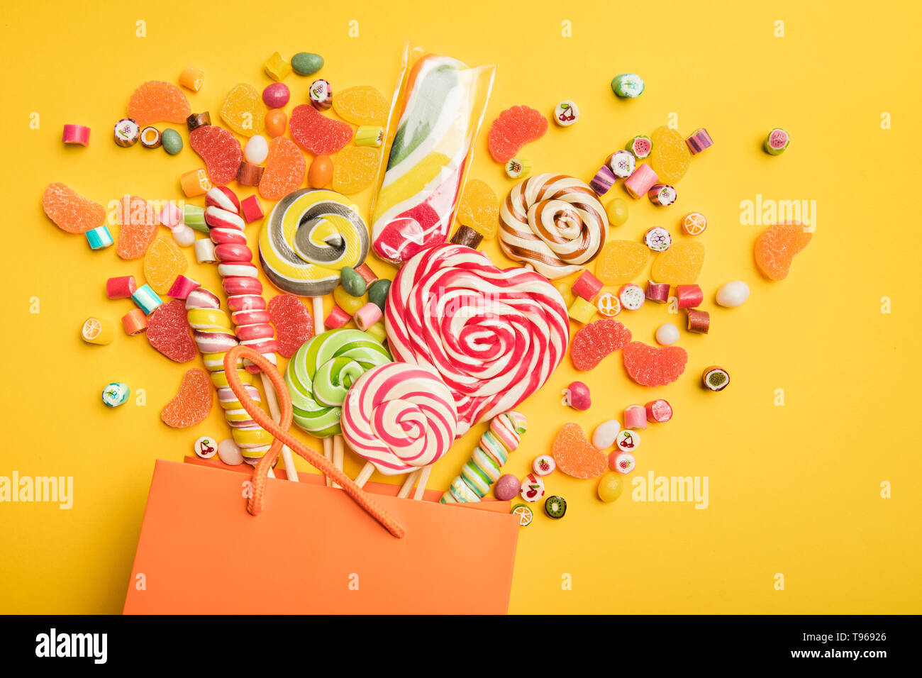 top view of tasty multicolored sweets scattered from paper bag on bright yellow background Stock Photo