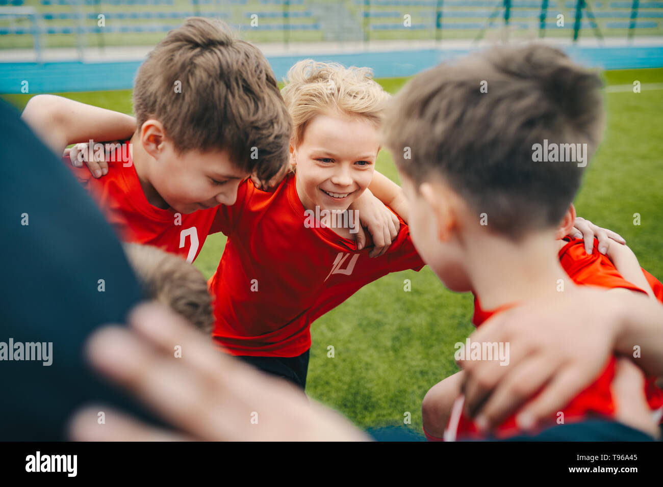 Happy children making sport. Group of happy boys making sports huddle. Smiling kids standing together with coach on grass sports field. Boys talking w Stock Photo