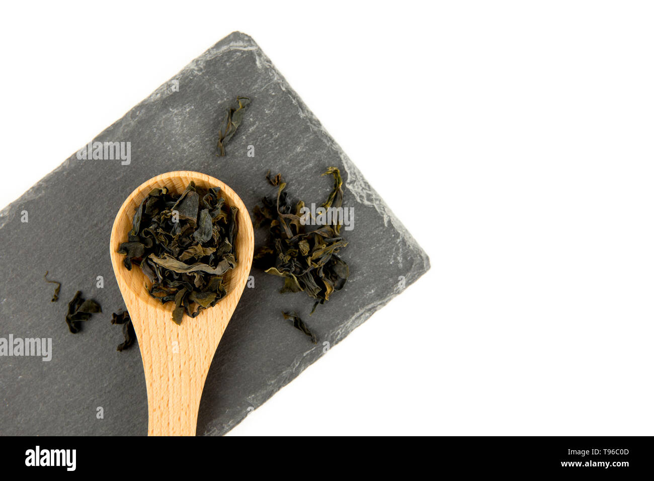 Small pieces of dried Wakame (Undaria pinnatifida), edible seaweed, ingredient to different foods in wooden spoon on black stone cutting board isolate Stock Photo