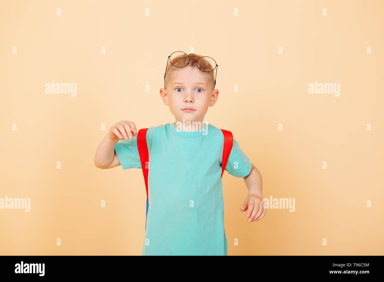 Little funny boy standing in the studio with glasses, backpack. Surprising. Isolated on the yellow. Concept school Stock Photo