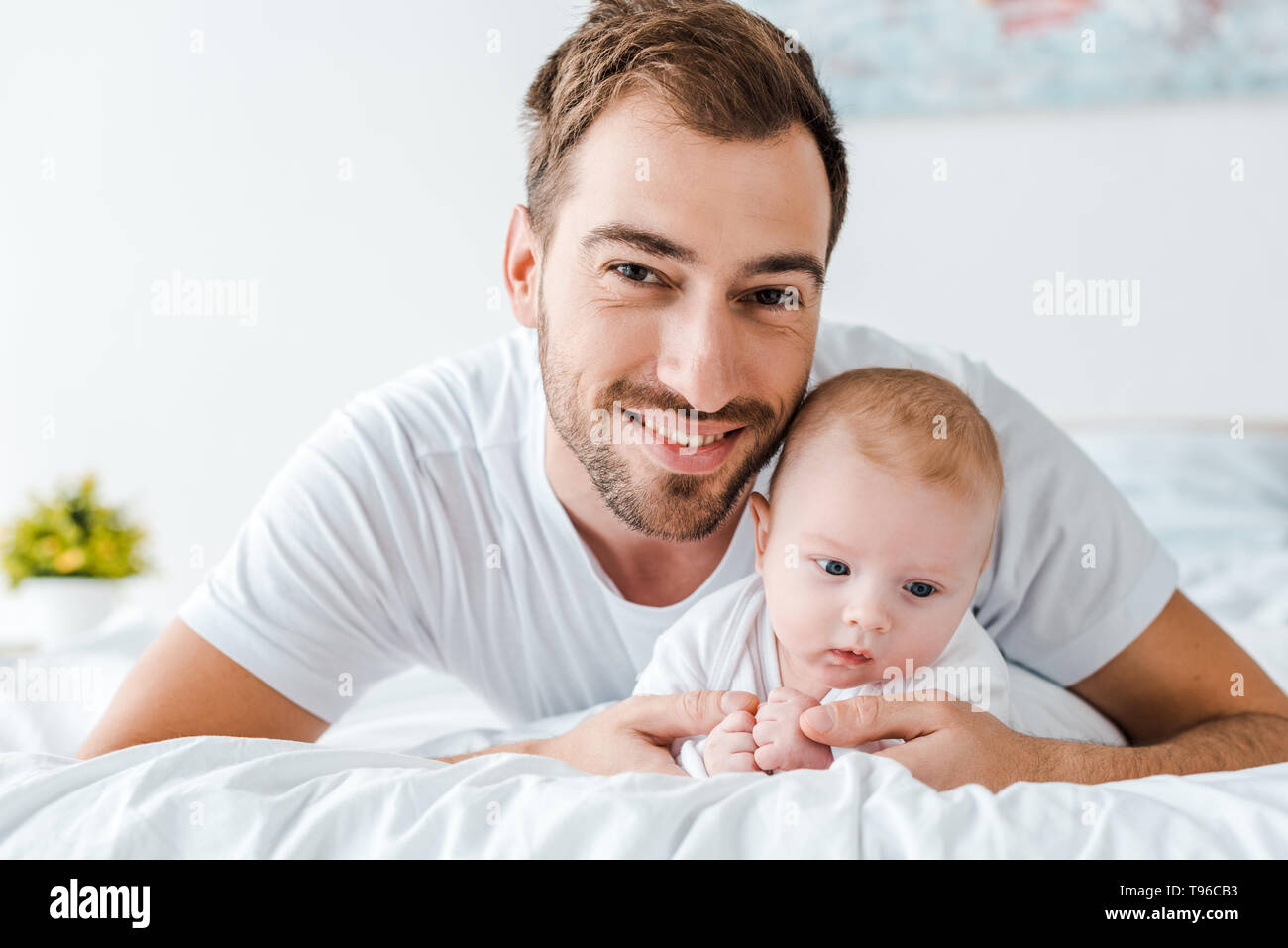 Smiling father lying on bed with baby in bedroom Stock Photo - Alamy