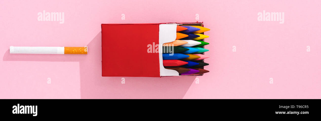 panoramic shot of colorful crayons in cigarette pack and tobacco cigarette  on pink, smoking concept Stock Photo