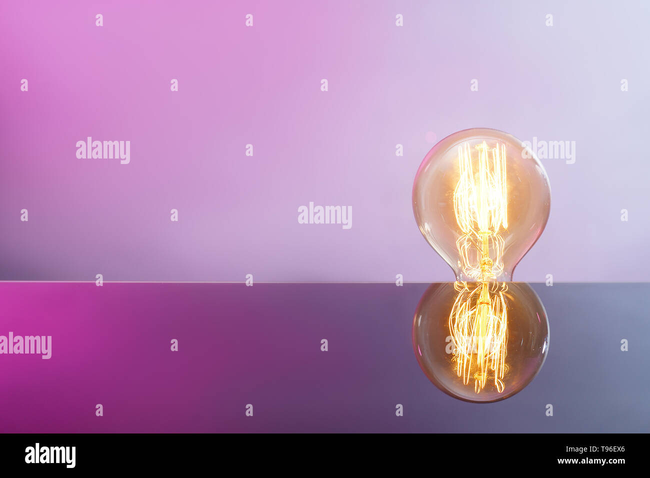 Glowing retro light bulb with reflection on color background Stock Photo
