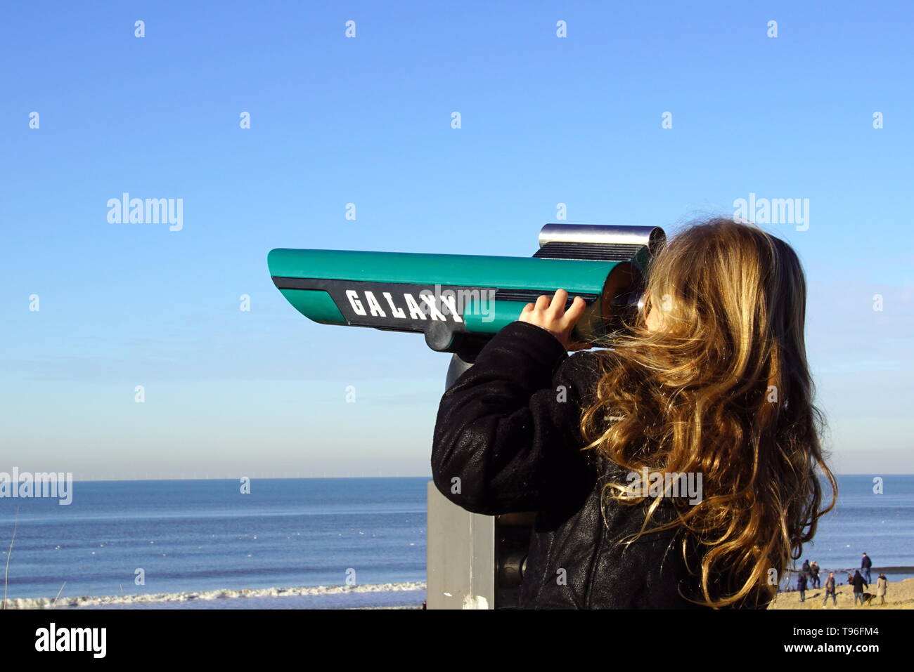 Blond girl looks through tourist binoculars against a blue sky. Stock Photo