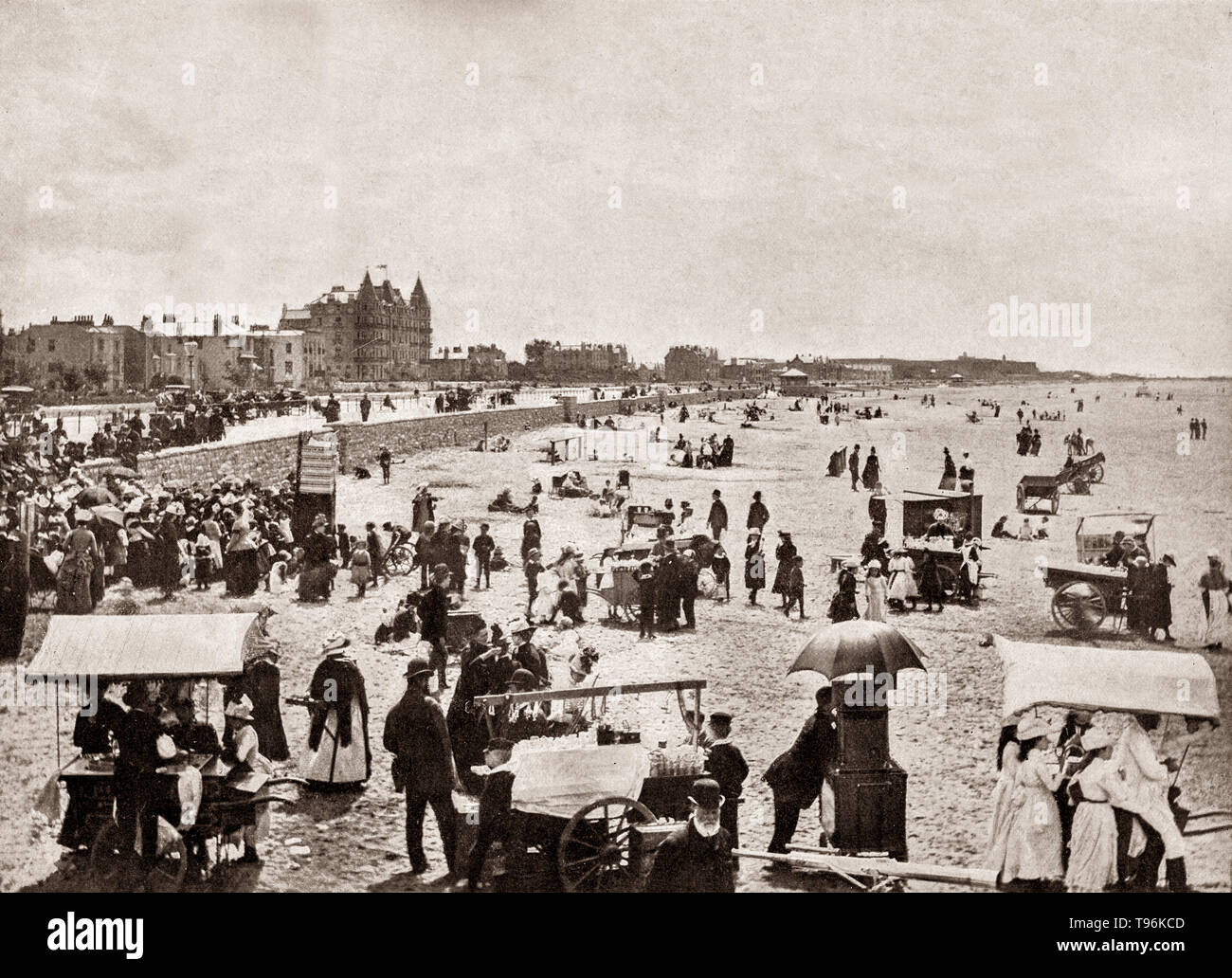 A late 19th Century view of a crowded beach at Weston-Super-Mare, aka Weston, a seaside town on the Bristol Channel in North Somerset, England. Early in the 19th century, Weston was a small village of about 30 houses, located behind a line of sand dunes fronting the sea, and grew with the Victorian era boom in seaside holidays.  Mining families came across the Bristol Channel from South Wales by paddle steamer to enjoy its beach,  amusement arcades, tea rooms, amusement rides and a photographic studio. Stock Photo