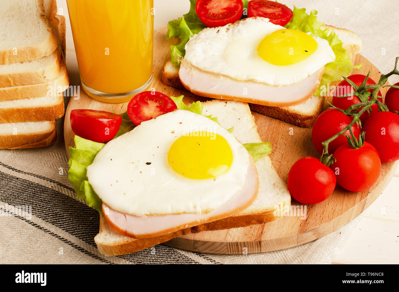 Ham sandwich with scrambled egg, tomato, lettuce, delicious healthy breakfast and orange juice on white wooden background Stock Photo