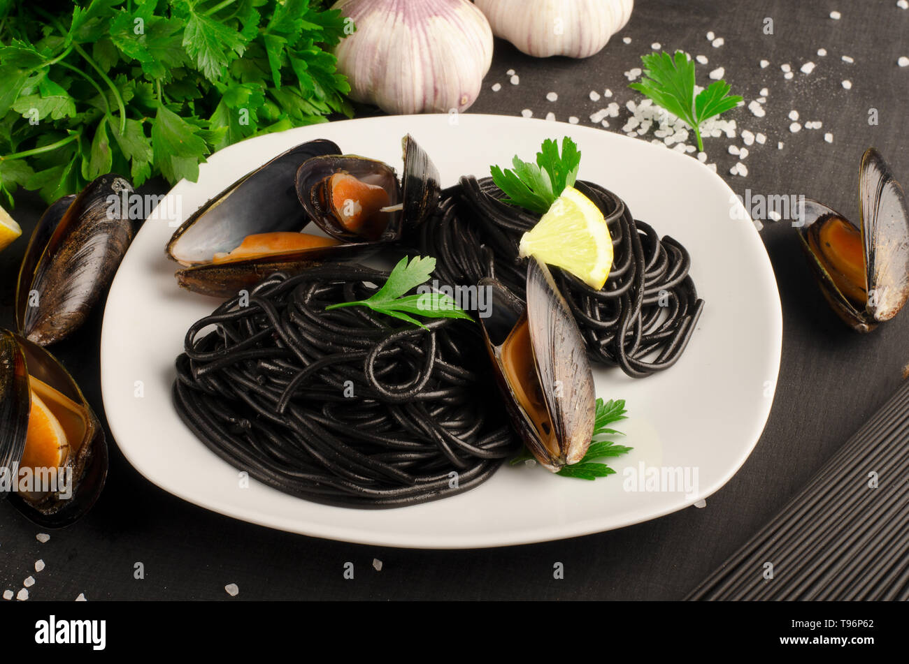 Seafood black pasta spaghetti with mussels on white plate on dark background.  Mediterranean delicacy food Stock Photo
