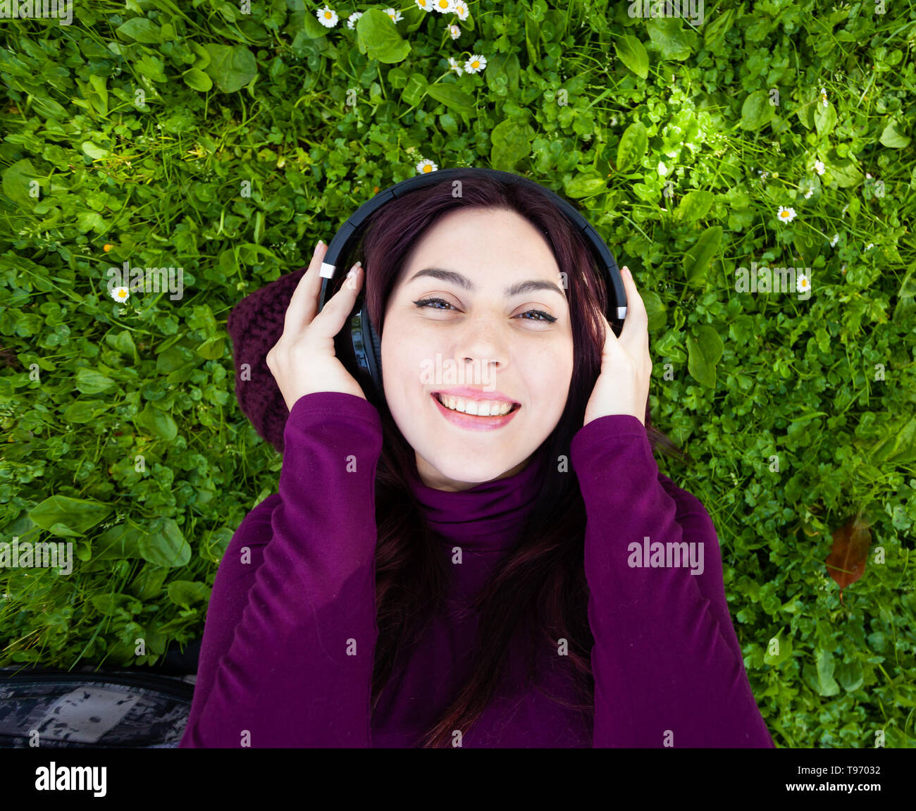 Young beautiful girl laying on the grass in park listening to music with headphones. Top view and copyspace. Stock Photo