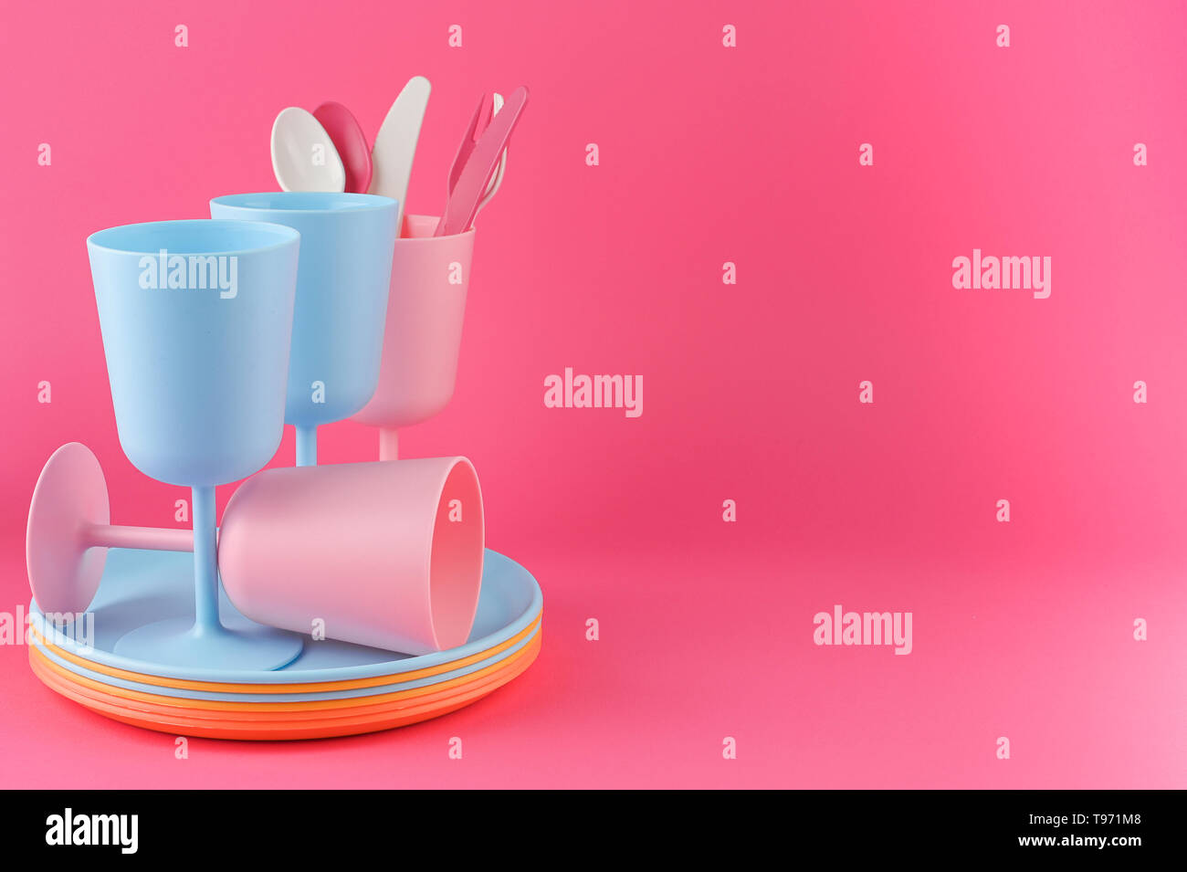 Colored plastic picnic utensils in bright colors. Glasses and plates in