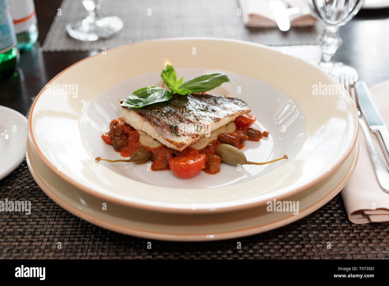 Sea bass fillet with tomato sauce and capers, place setting of a restaurant Stock Photo