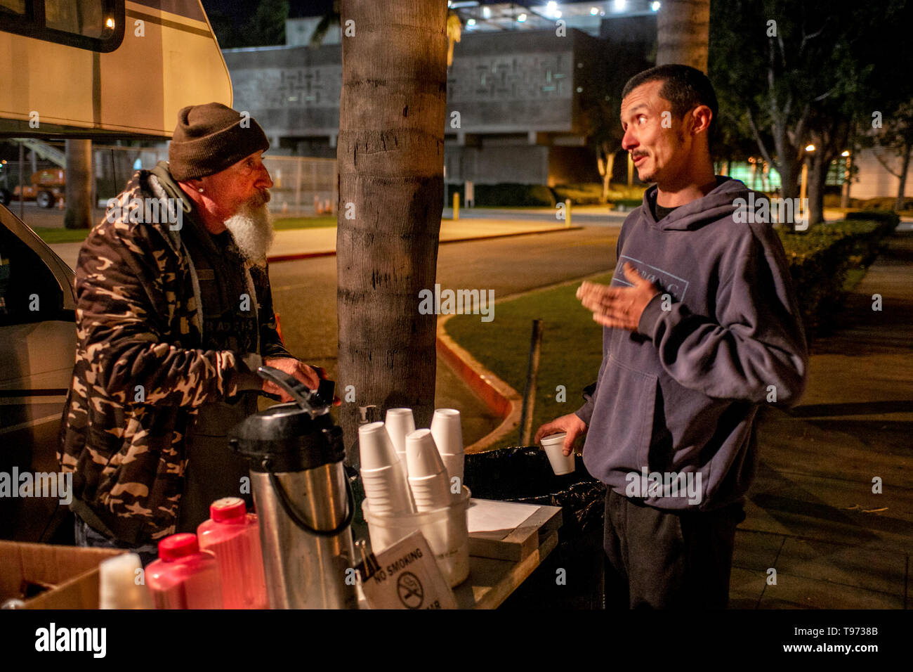 A bearded volunteer helps a released prisoner with food and support from a van parked outside a county jail at night in Santa Ana, CA. Stock Photo