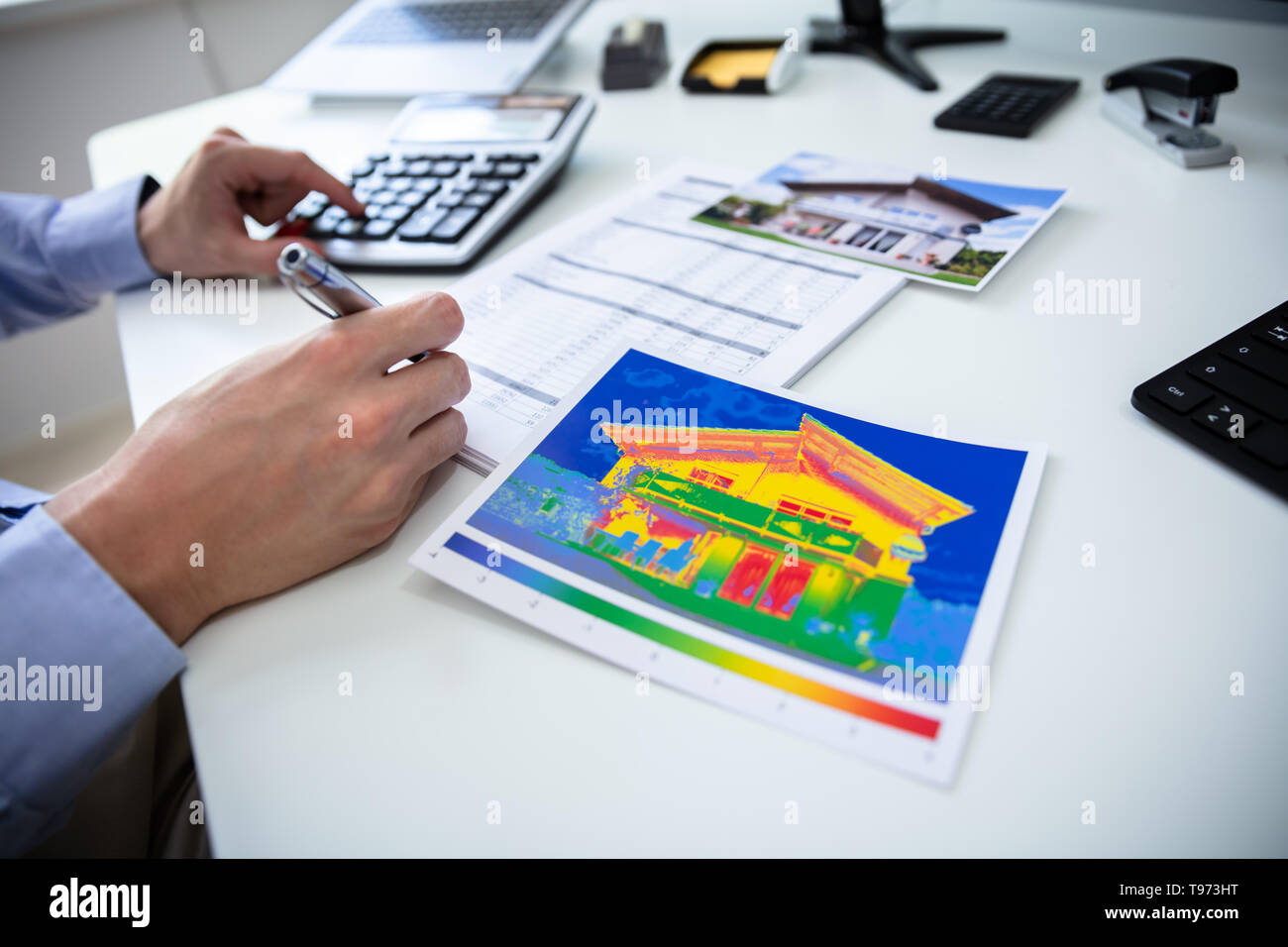 Close-up Of Person Hand Calculating Heat Temperature Using Calculator On Desk Stock Photo