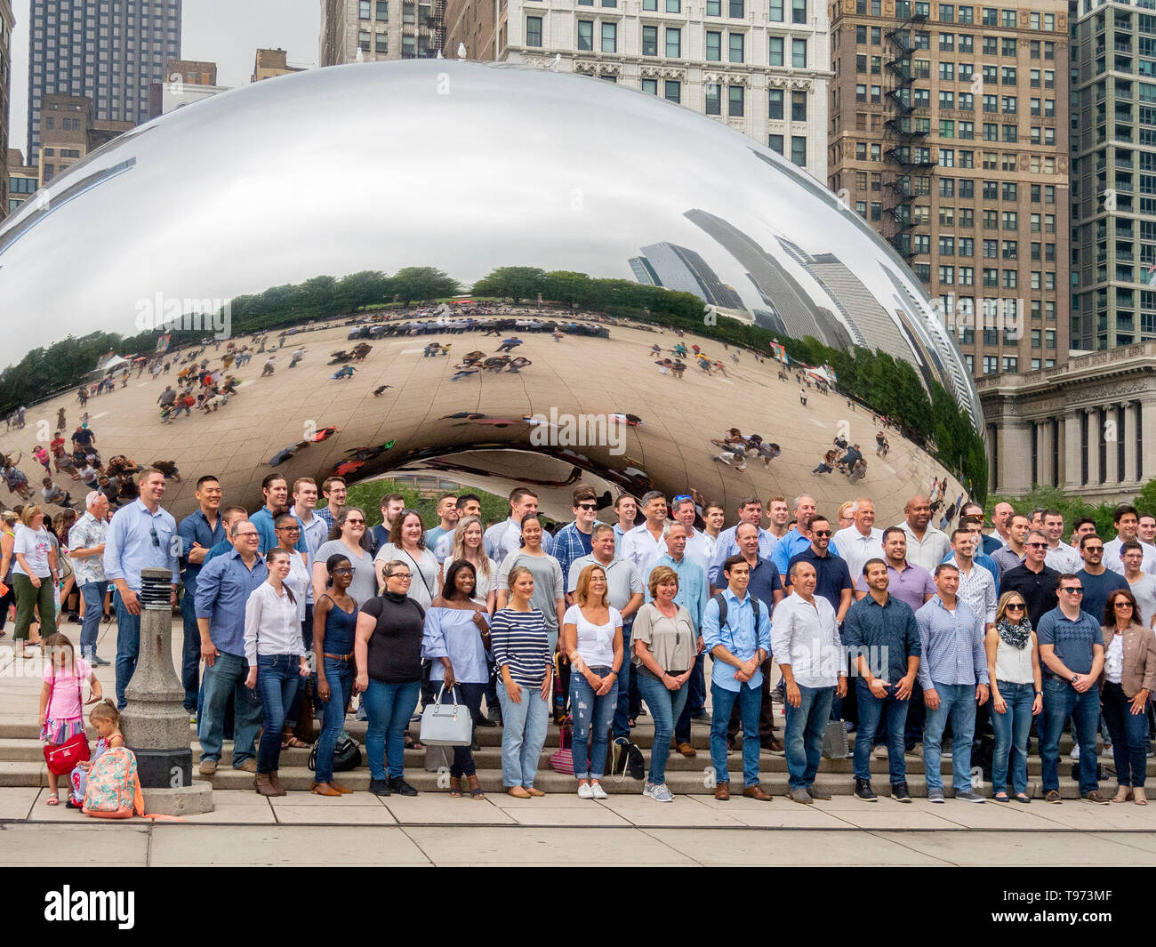 Tourists pose for a group photo at Cloud Gate in Millenium Park, Chicago. Cloud Gate is a public sculpture by Indian-born British artist Sir Anish Kapoor, that is the centerpiece of AT&T Plaza at Millennium Park in the Loop community area. Stock Photo