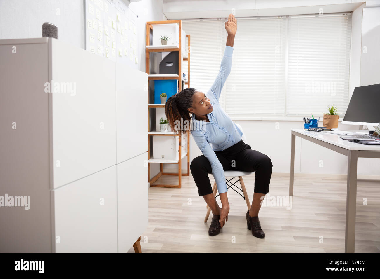 Young Businesswoman Doing Yoga Standing In Front Of Office Desk