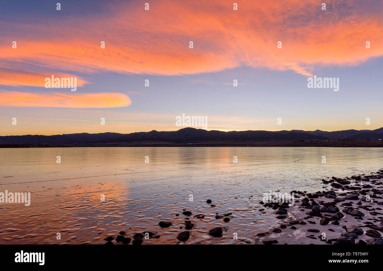 Orange Clouds - Bright orange color sunset clouds rolling over frozen Chatfield Reservoir at foothill of front range of Rocky Mountains. Colorado, USA. Stock Photo