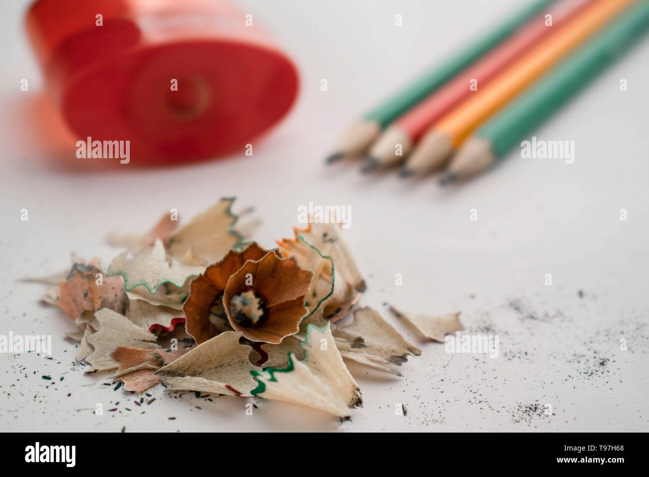 on the background lie red large oval sharpener, colored ground pencils that indicate on a pile of sawdust lying in the foreground, white background Stock Photo