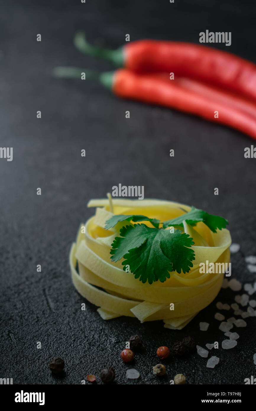 on a dark background raw fettuccine paste wrapped in a ball with fresh green cilantro leaves with coarse sea salt, black and red peppercorns and whole Stock Photo